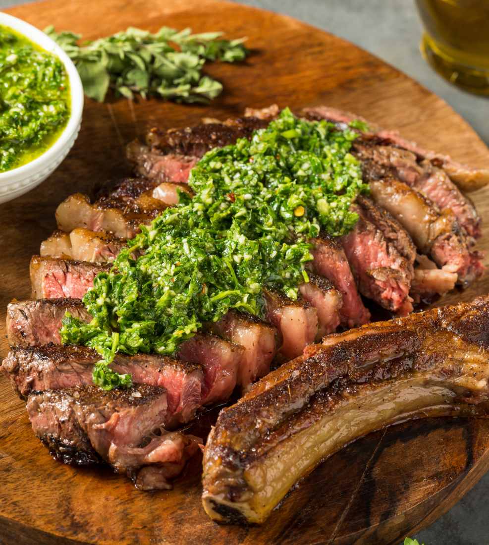 a sliced steak with green sauce on a wooden board