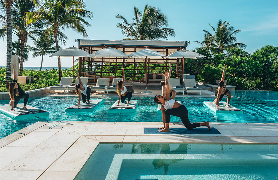 group of women doing yoga on floating platforms on a pool